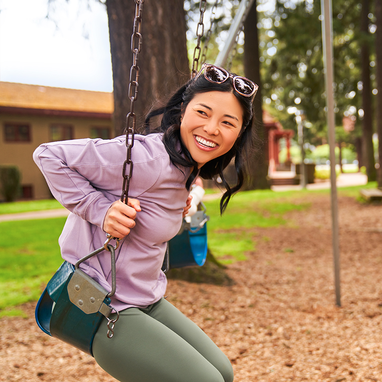 A smiling woman swings on a swing set at a playground.