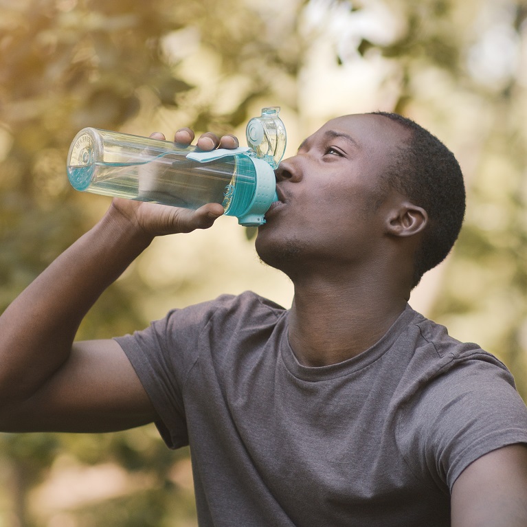 Un homme assis à l’extérieur boit d’une bouteille d’eau réutilisable.