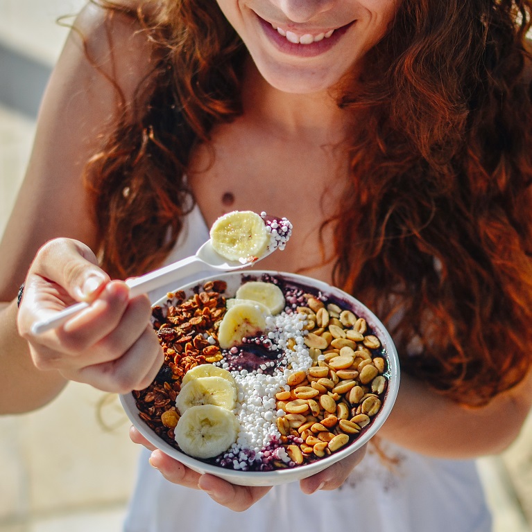 Une femme souriante aux longs cheveux tient un bol rempli d’aliments nutritifs.